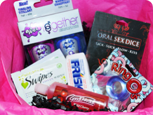 Photo of the Luv My Box November contents in pink wrapping paper. The package includes a tube of Good Head gel, some Swipes individually-wrapped clean-up wipes, a Screaming O cock ring, Wet's "His" and "Her" [gendering theirs, not mine] warming and cooling lube, Frisk mints in a plastic container, and a package of oral sex dixe.