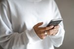 CC0 photo of a white person in an oversized white hoodie holding a smartphone in both hands.