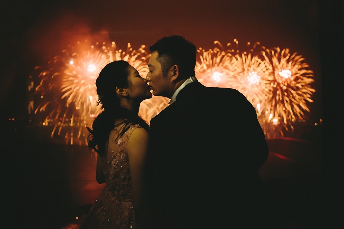 Photo of 2 Chinese people in formal attire kissing in front of beautiful golden fireworks