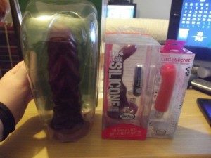 Photo of 3 sex toys still in their packaging lined up in a row: the Pleasure Works Rippler, the Tantus ProTouch, and the Tantus Little Secret Spoon.
