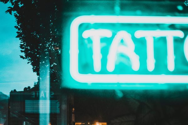 Photo of the window of a tattoo parlor, a green neon sign drawing the eye, though only half is visible - it's the first half of the word "Tattoo"