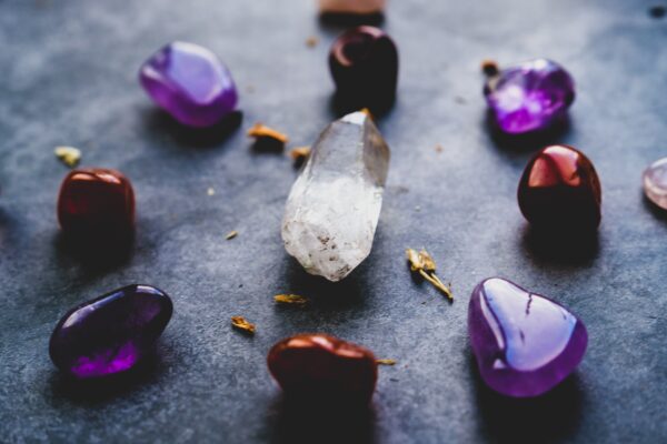 Photo by Dan Farrell on Unsplash of tumbled amethyst and carnelian stones surrounding a rough piece of quartz.