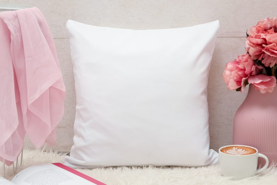 Photo of a white fur rug surrounded by a white pillow, pink scarves, a pink vase with lovely pink flowers, showcasing an open book and mug of coffee with a pretty milk design drawn across the top of the cup.